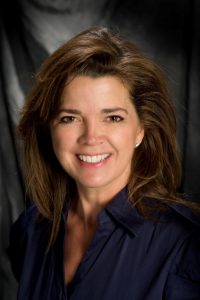 A woman in a navy blouse smiling cheerfully at the camera.