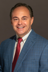 A man wearing a checkered blue suit, smiling confidently at the camera