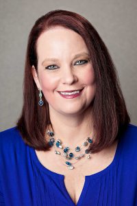 A woman wearing a blue blouse, smiling brightly at the camera.