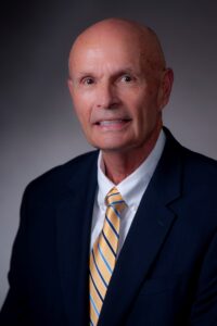 A man with a friendly smile wearing a striped tie, looking directly at the camera. Jack