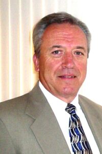 A man wearing a gray suit jacket and a white shirt, smiling at the camera. Barry Bridges