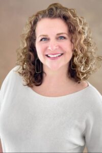 A woman with curly hair and blue eyes, smiling warmly at the camera. Ashley Donahue